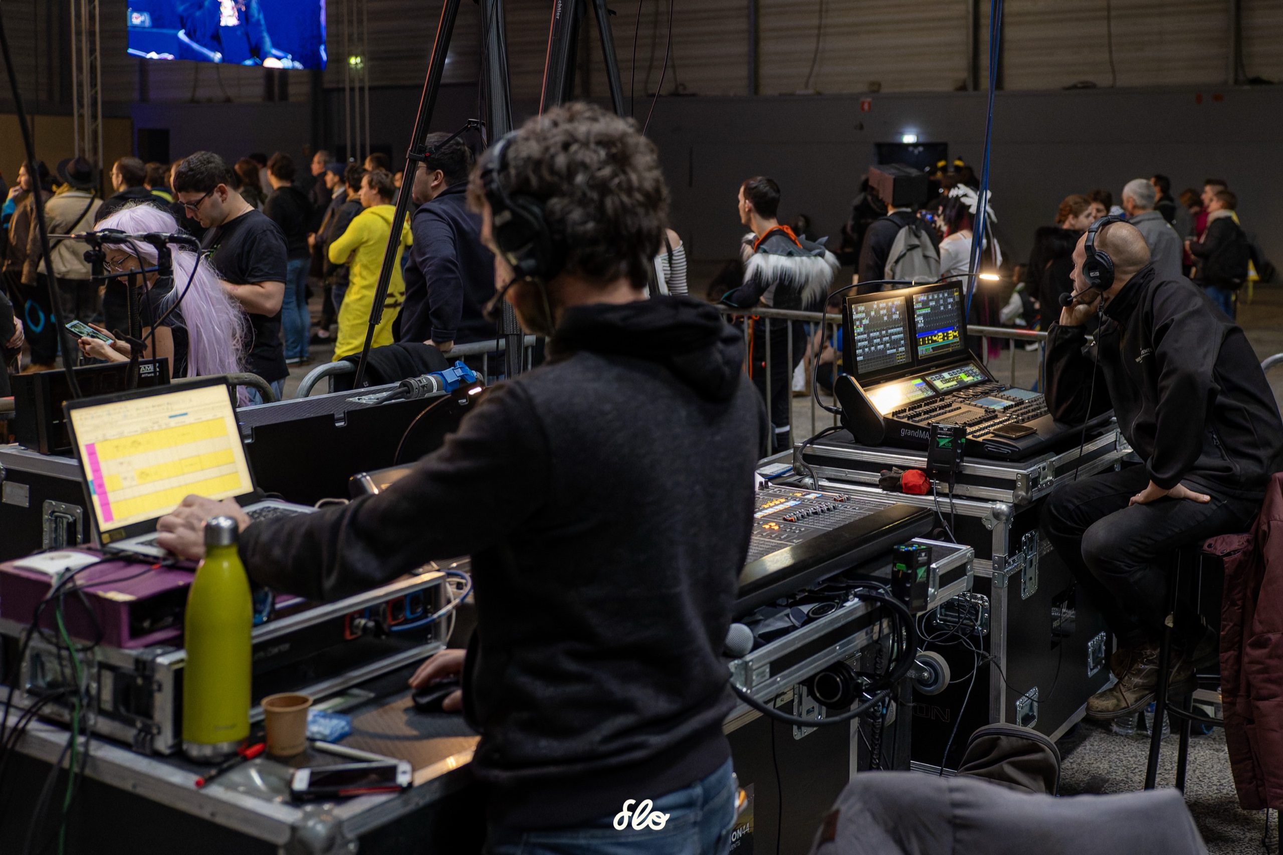 Technicien de régie vu de dos devant ses écrans de contrôle, public et scène du salon Art To Play en arrière-plan