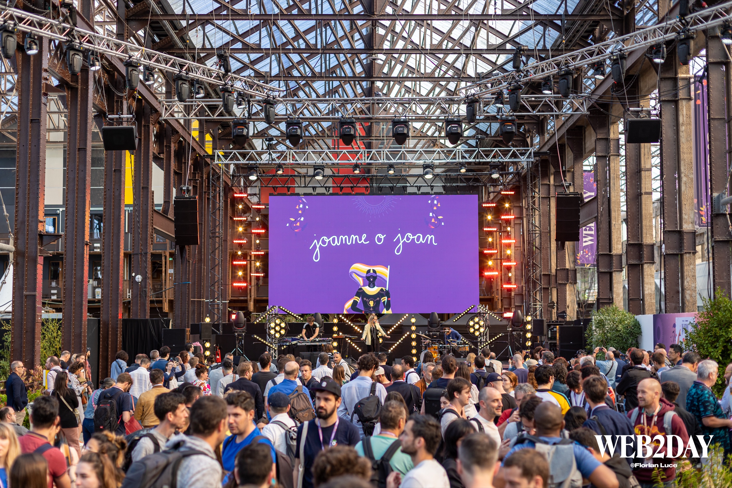 Foule de visiteurs sous la charpente métallique des Nefs de Nantes lors du festival Web2day, écran géant et lumières de scène