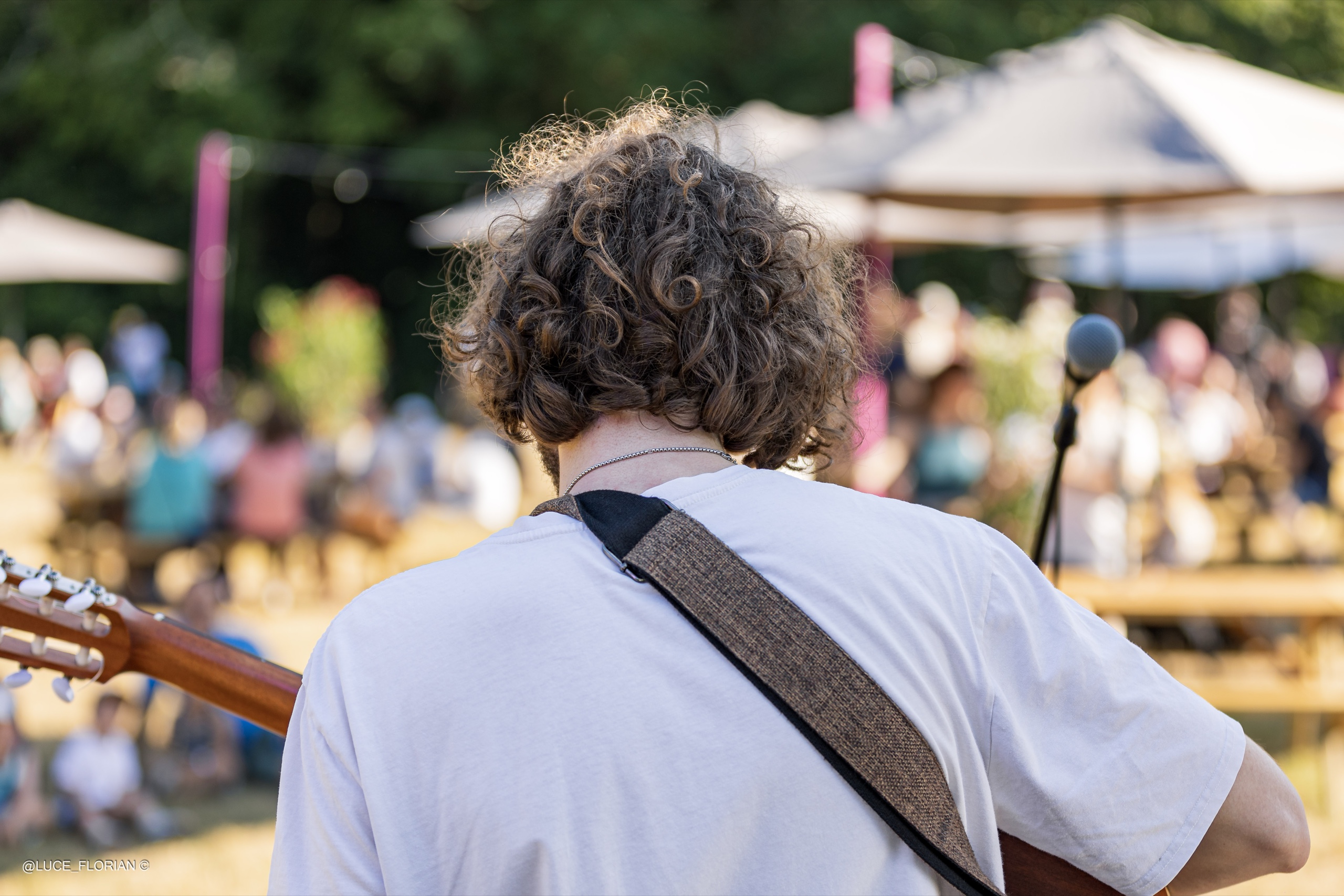 Le guitariste chanteur Nomah, vu de dos face au public d'une guinguette en plein air, lumière dorée de fin de journée