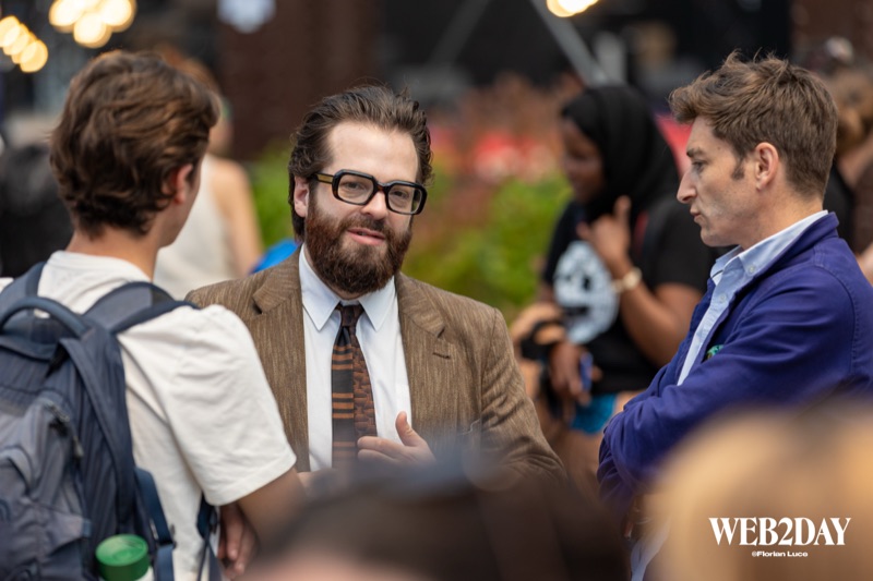 Trois professionnels échangeant debout lors d'un moment de networking, arrière-plan flou coloré