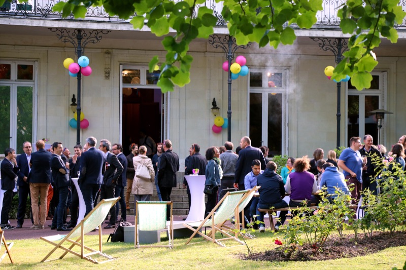 Cocktail corporate en extérieur devant un manoir, invités en costume, ballons colorés et transats sur la pelouse