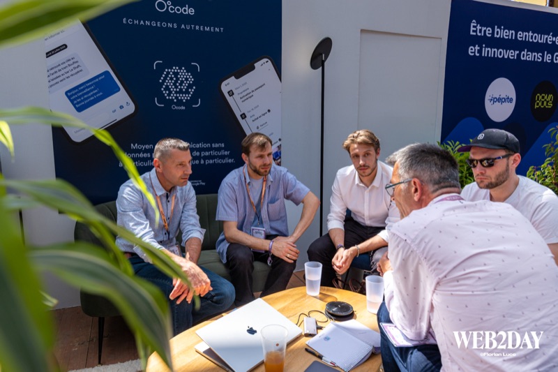 Quatre professionnels en discussion autour d'une table basse sur le stand O'code, feuillage en premier plan