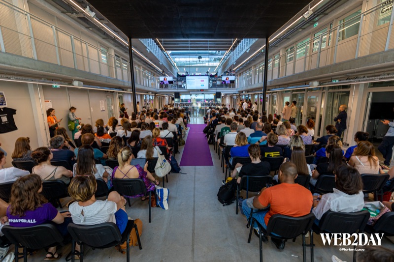Salle comble vue de dos, public assis face à une scène avec allée centrale violette