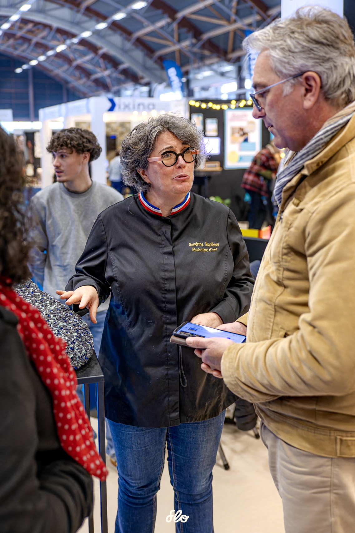 L\'artisane Sandrine Morilleaude titrée meilleur ouvrière de France mosaïste d\'art, en veste noire au col tricolore échangeant avec un visiteur au Salon Habitat d'ExpoNantes