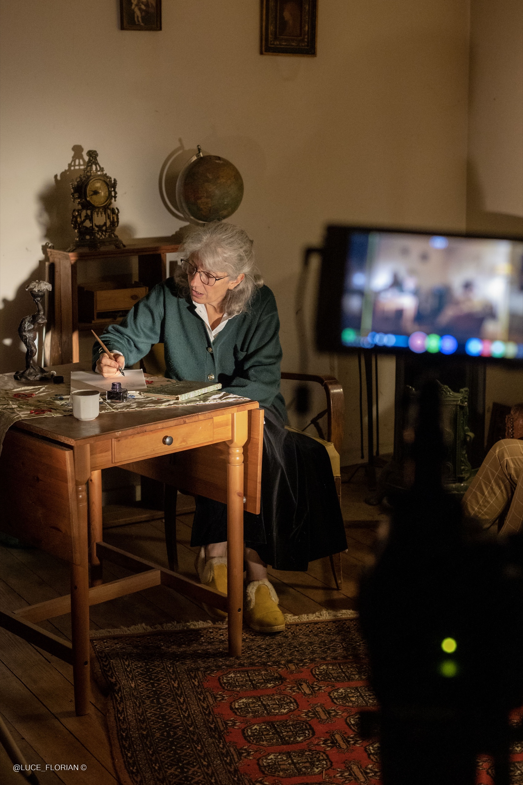 Actrice écrivant à un bureau sous un éclairage intimiste, moniteur de tournage au premier plan