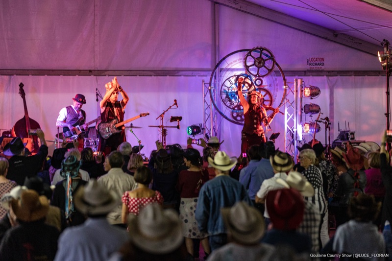 Groupe steampunk Crazy Pug sur scène devant un public en chapeaux cowboy, éclairage violet et décor d'engrenages