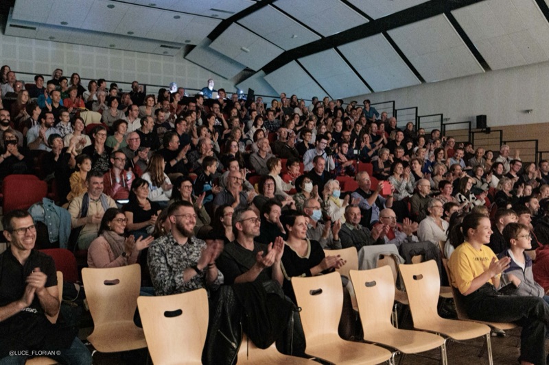 Public applaudissant dans les gradins d'une salle de spectacle comble
