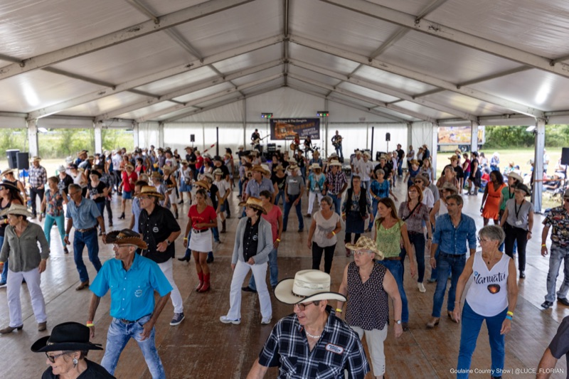 Danseurs de country en line dance sous un grand chapiteau, groupe sur scène en arrière-plan
