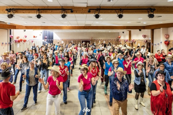 Vue en hauteur de la salle comble avec danseurs en lignes, chapeaux de cowboy et tenues colorées