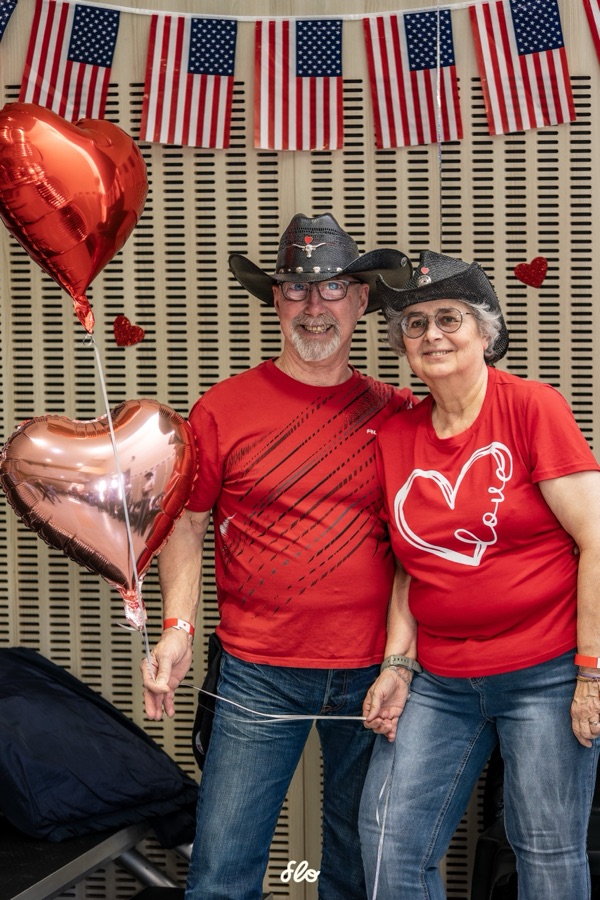 Couple en tenues rouges et chapeaux noirs posant avec des ballons cœur et drapeaux américains