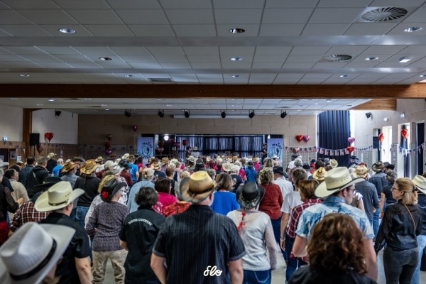 Vue de dos des danseurs face à la scène, salle remplie de chapeaux de cowboy