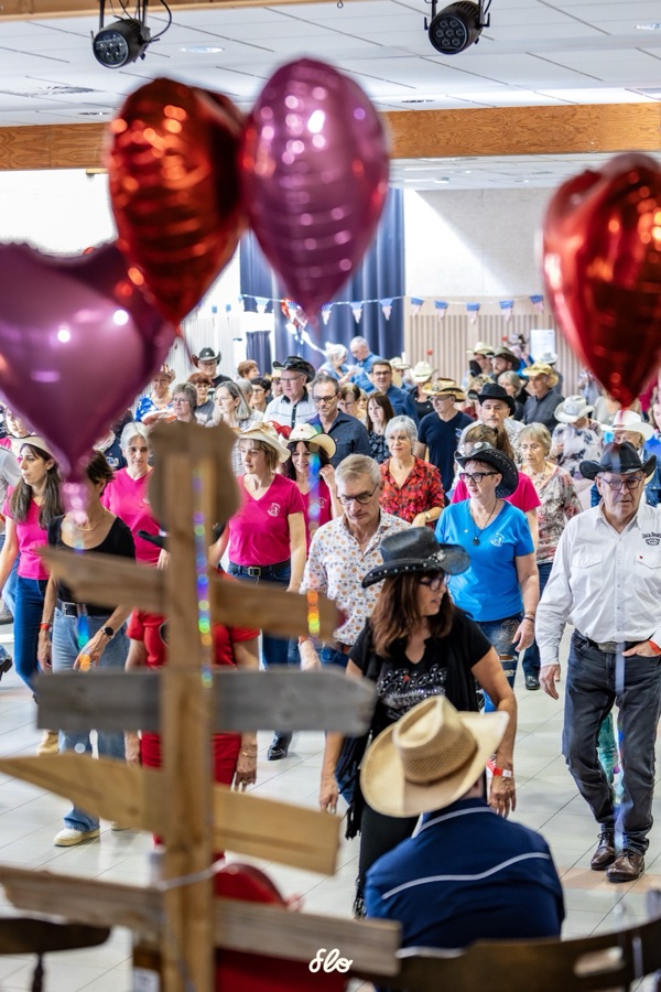 Danseurs avançant vus à travers une croix en bois décorative et des ballons en forme de cœur