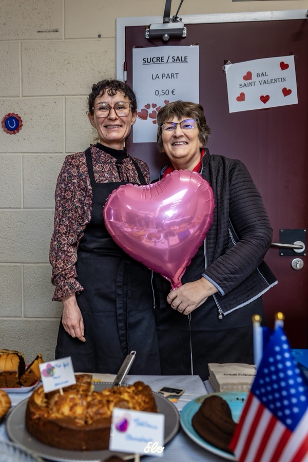 Deux bénévoles posant avec un ballon cœur rose devant la table de gâteaux et drapeaux américains
