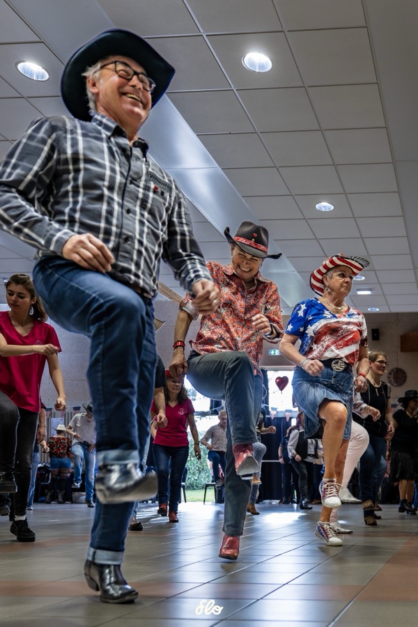 Trois danseurs en bottes et chapeaux levant la jambe en rythme, sourires aux lèvres