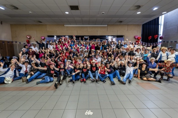 Photo de groupe de l'ensemble des participants bras levés dans la salle, près de 180 danseurs