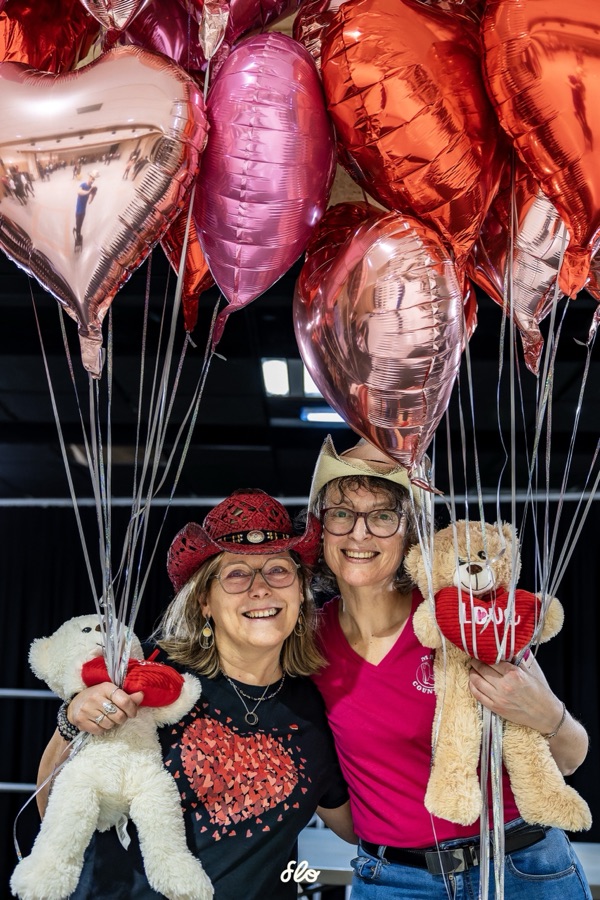 Deux participantes souriantes tenant des peluches sous une grappe de ballons cœur