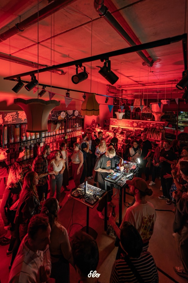 Vue en hauteur du magasin transformé en salle de concert, public massé autour du DJ sous éclairage rouge