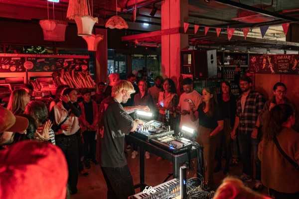 Vue large du DJ entouré du public en cercle, guirlandes suspendues et rayons du magasin en fond