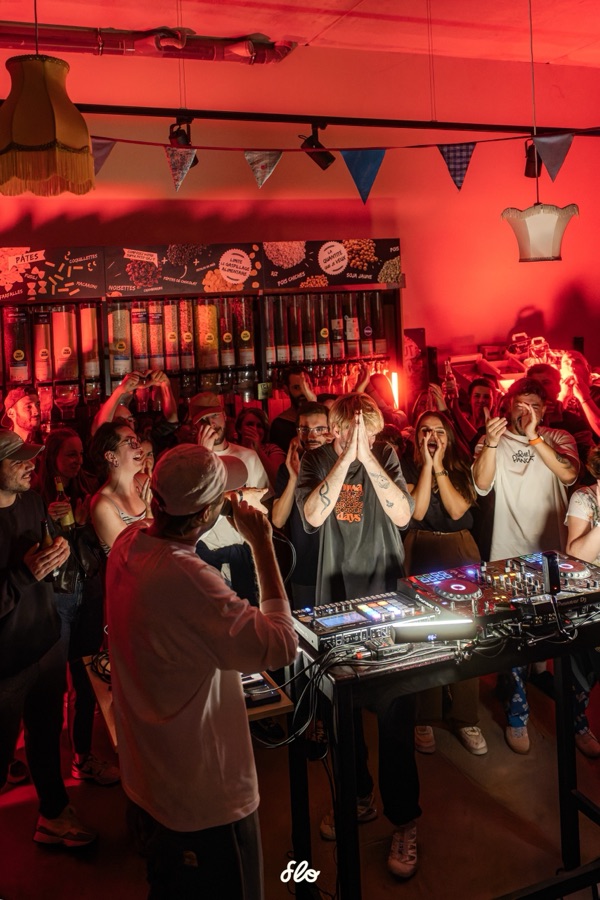 Public applaudissant face au DJ, mains levées, abat-jours et guirlandes en arrière-plan