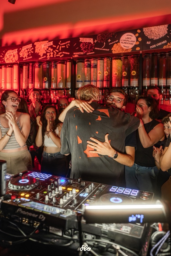 Accolade entre Fakear et un proche derrière les platines, spectateurs applaudissant autour